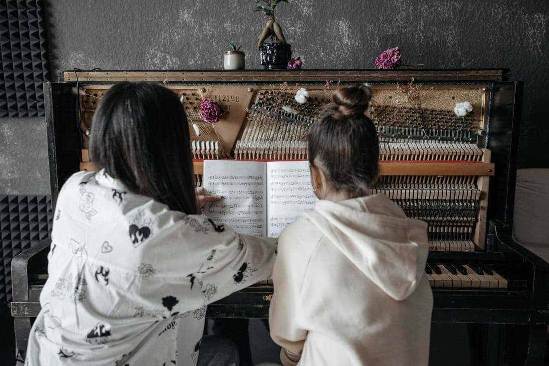 Two students reading music together at an upright piano