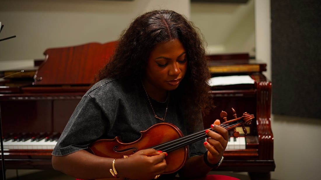 Aanu Adeyemo playing the violin beside a grand piano