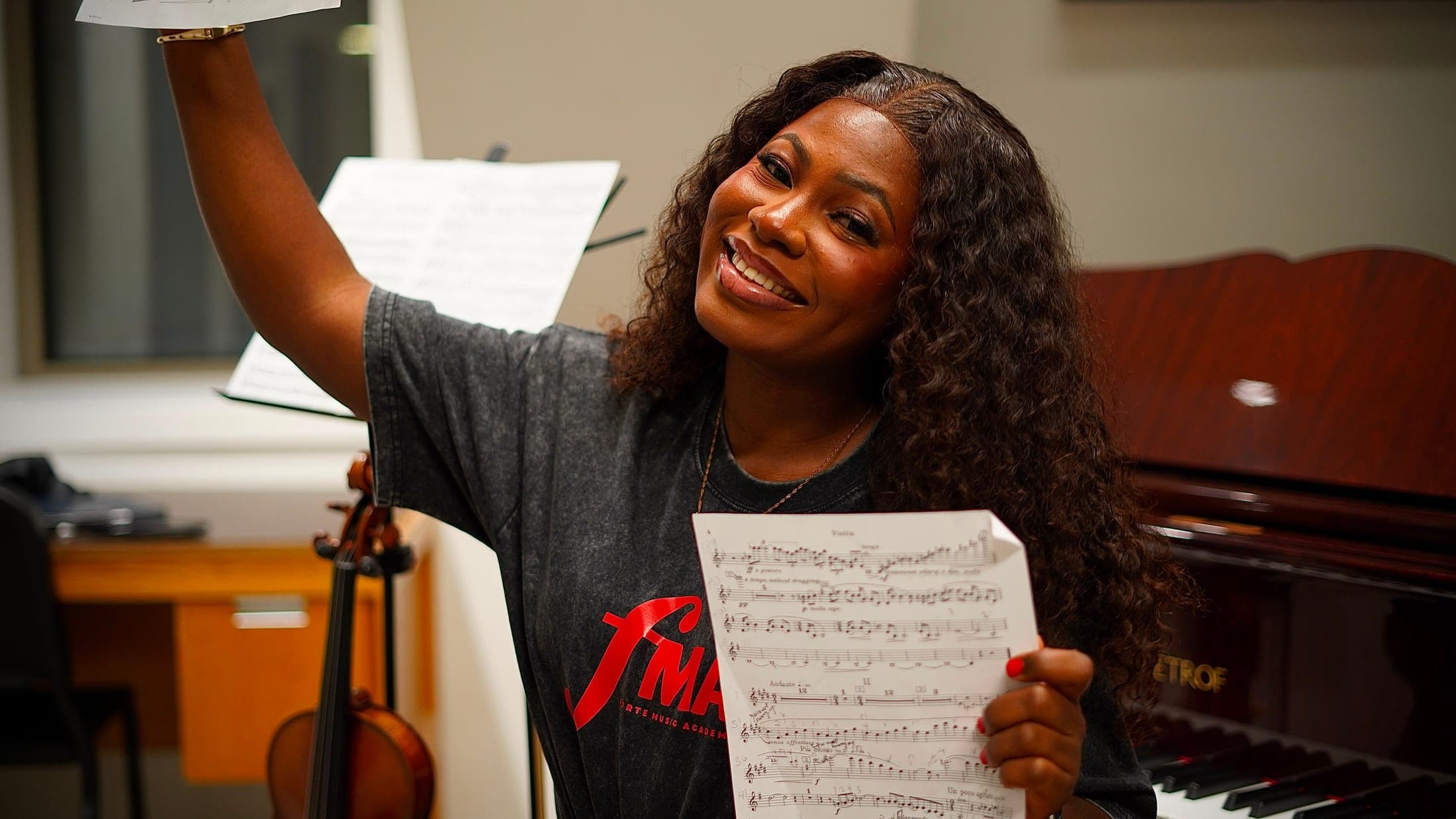 Aanu Adeyemo in an FMA tee, sheet music in hand, beside a violin and piano